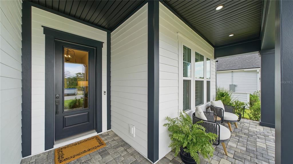A covered front porch with white siding, dark trim, a glass-paneled door, and two chairs — 203 TESORO TERRACE, ST AUGUSTINE, FL