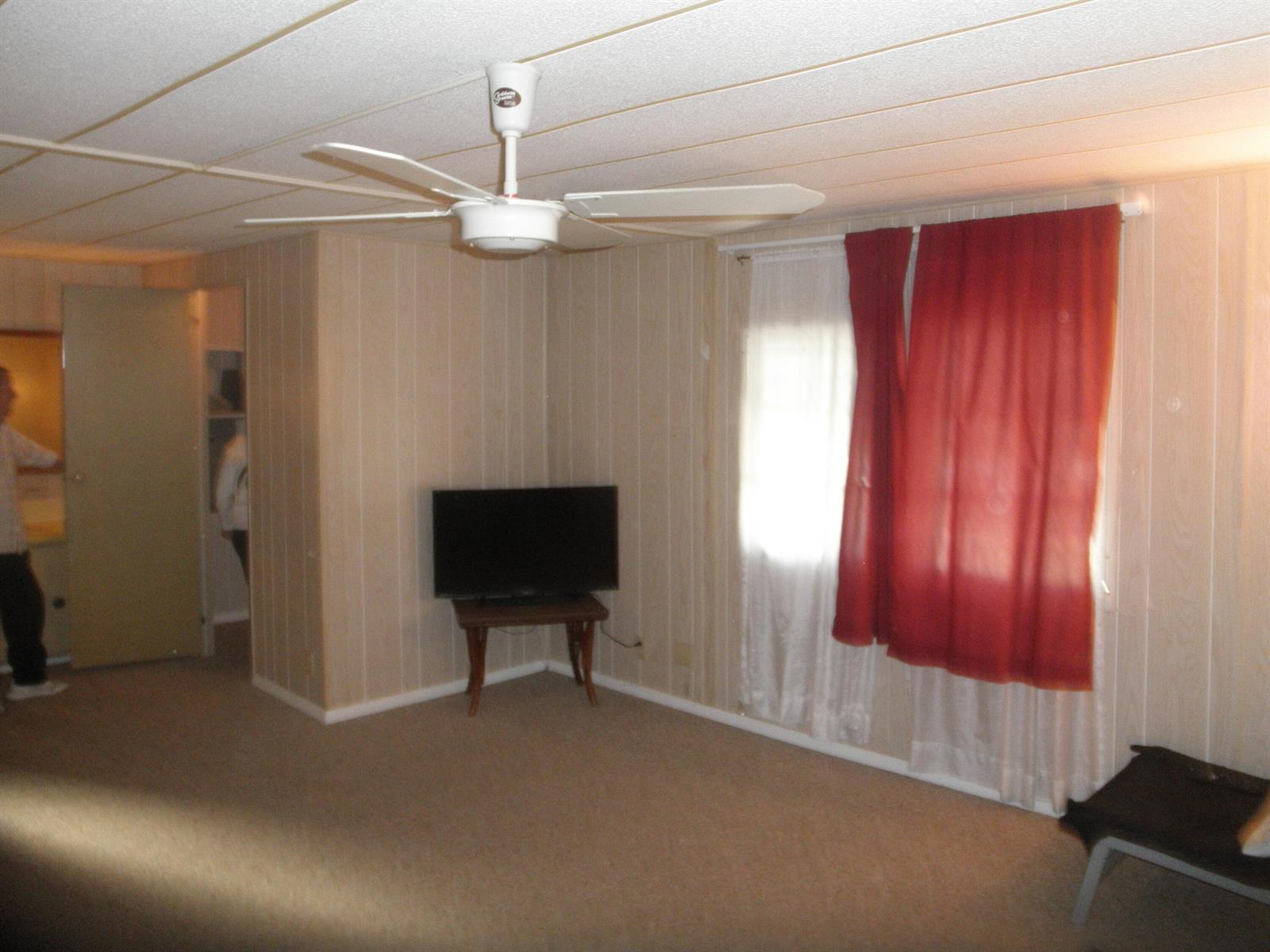 A room with wood-paneled walls, beige carpet, a ceiling fan, and a television on a stand — 4544 Sunset Ranch Road, West Palm Beach FL 33415, WEST PALM BEACH, FL