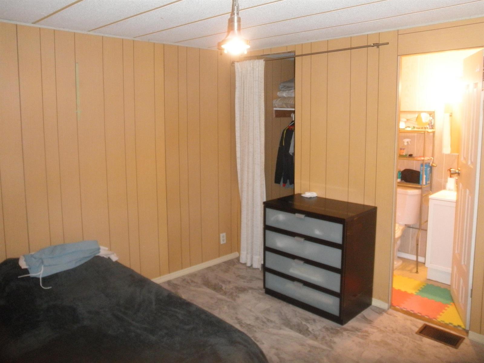 A bedroom with wood-paneled walls, a dark dresser, a curtained closet, and an attached bathroom — 4544 Sunset Ranch Road, West Palm Beach FL 33415, WEST PALM BEACH, FL