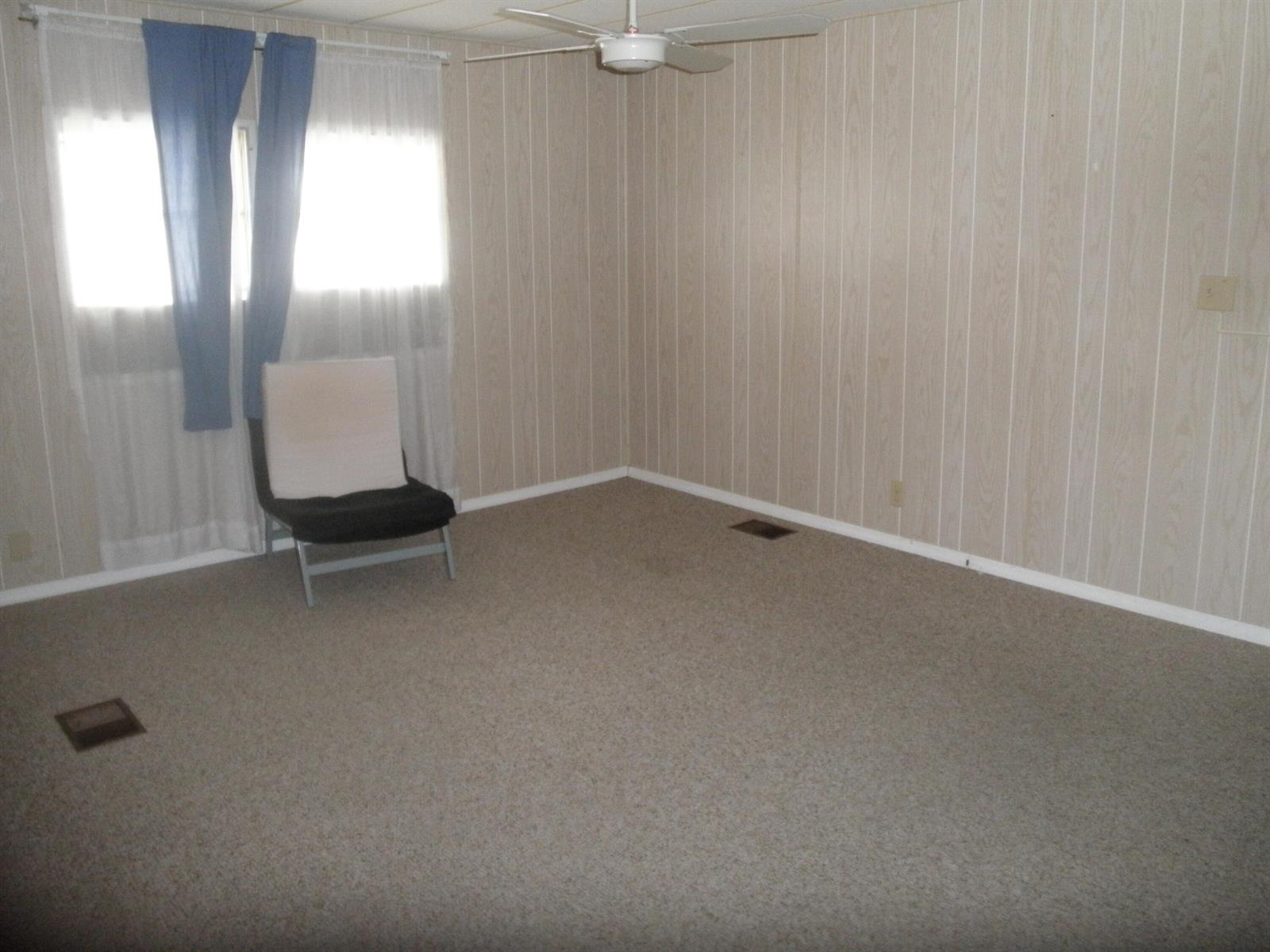 An empty room features wood-paneled walls, beige carpeting, a ceiling fan, and a single chair — 4544 Sunset Ranch Road, West Palm Beach FL 33415, WEST PALM BEACH, FL