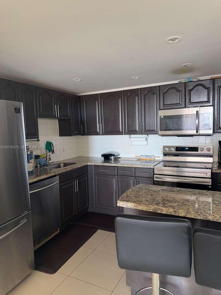 A kitchen features dark wood cabinets, granite countertops, and stainless steel appliances — 13499 Biscayne Blvd # 906, North Miami FL 33181, NORTH MIAMI, FL