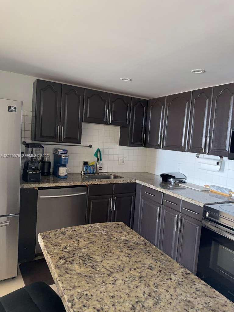 A kitchen features dark wood cabinets, granite countertops, and stainless steel appliances — 13499 Biscayne Blvd # 906, North Miami FL 33181, NORTH MIAMI, FL