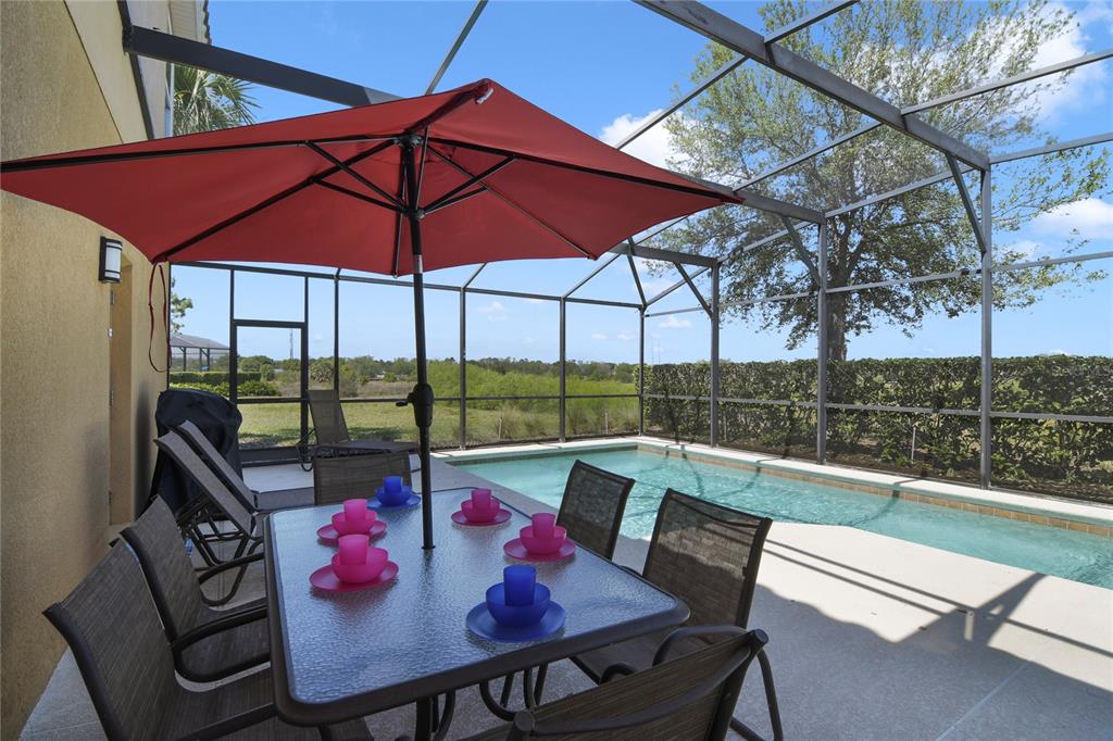 A patio with a dining set and umbrella overlooks a screened-in swimming pool and yard — 4115 OAKTREE DRIVE, DAVENPORT, FL