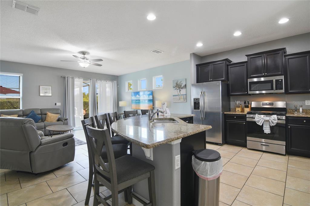 An open-concept kitchen and living area featuring dark cabinetry, granite countertops, and tile flooring — 4115 OAKTREE DRIVE, DAVENPORT, FL