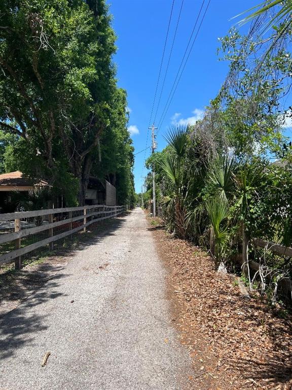 A narrow gravel path runs between a wooden fence and dense trees under a sky — 15617 CASEY ROAD, TAMPA, FL