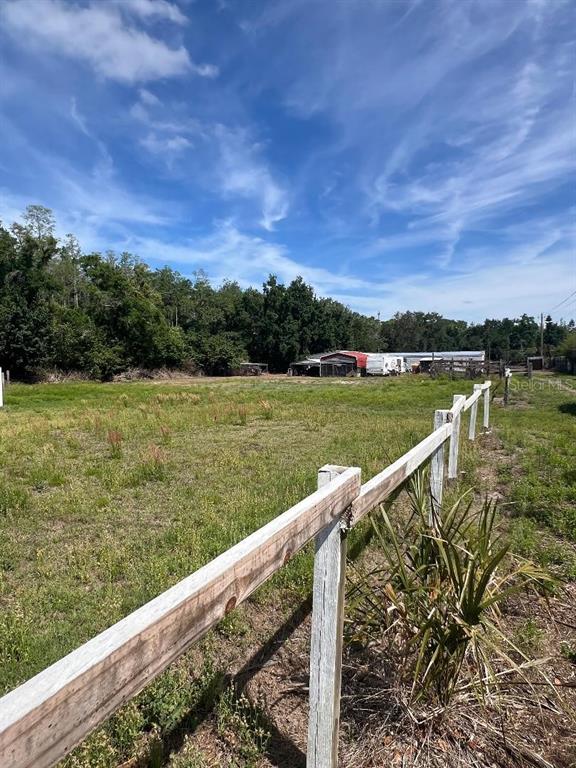 A wooden fence borders a grassy field with trees and outbuildings in the background — 15617 CASEY ROAD, TAMPA, FL