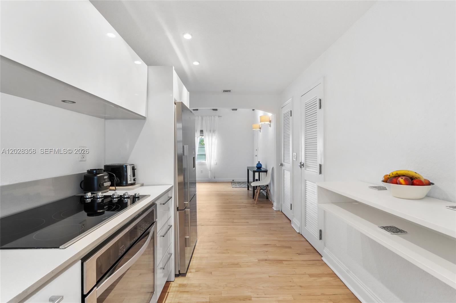 A modern kitchen with white cabinetry and stainless steel appliances opens into a living area — 1605 Euclid Ave # B1, Miami Beach FL 33139, MIAMI BEACH, FL