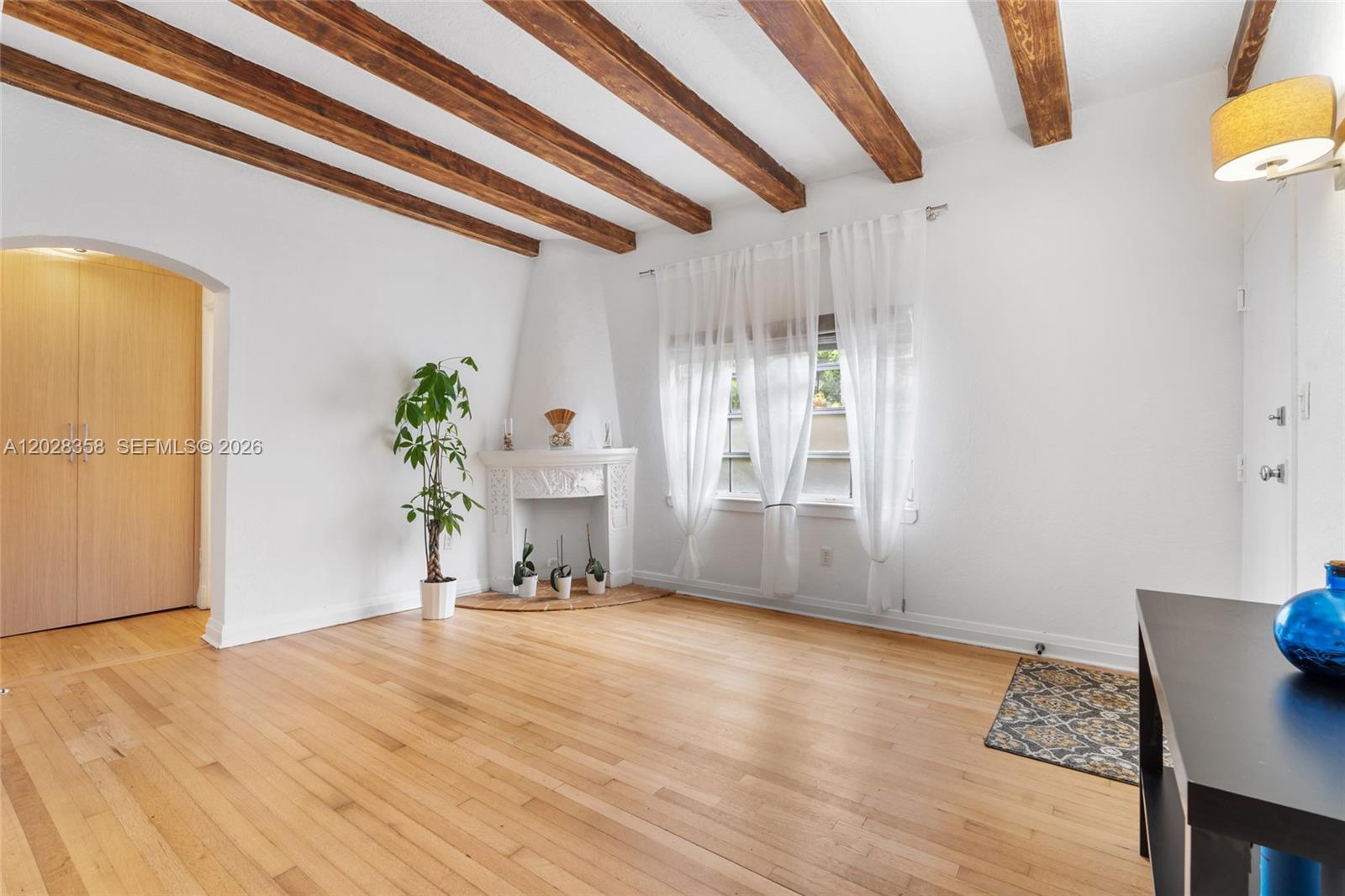 A living room features hardwood floors, exposed wooden ceiling beams, and a corner fireplace — 1605 Euclid Ave # B1, Miami Beach FL 33139, MIAMI BEACH, FL