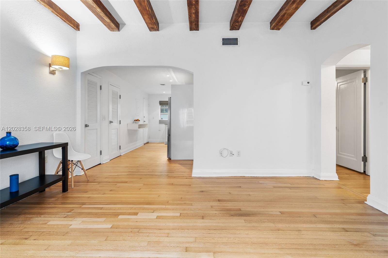 A bright living room features hardwood floors, exposed wood ceiling beams, and an arched entryway — 1605 Euclid Ave # B1, Miami Beach FL 33139, MIAMI BEACH, FL