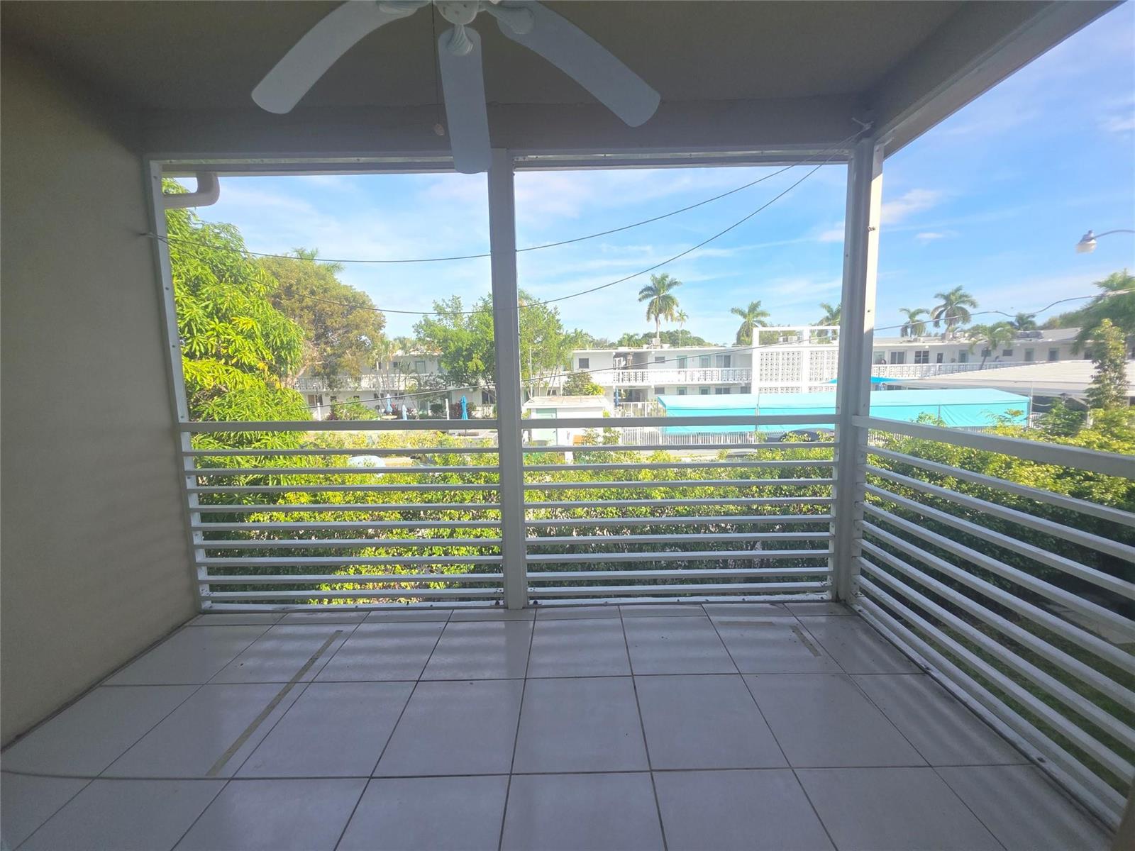 A tiled balcony features white horizontal railings, a ceiling fan, and views of surrounding buildings — 2131 NE 42nd Court # 209e, Lighthouse Point FL 33064, LIGHTHOUSE POINT, FL