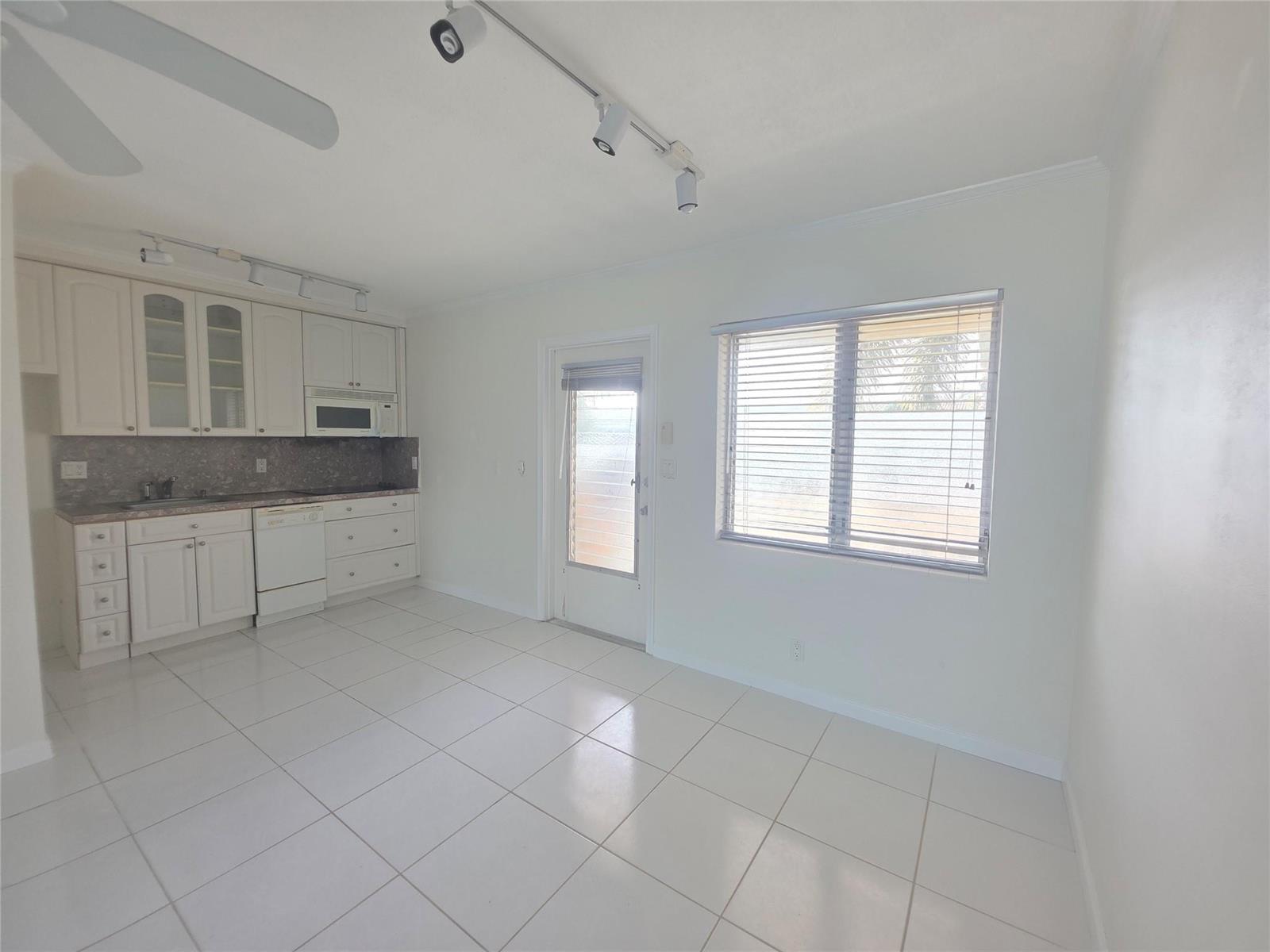 A kitchen with white cabinets, tile flooring, and a glass-paneled door next to a window — 2131 NE 42nd Court # 209e, Lighthouse Point FL 33064, LIGHTHOUSE POINT, FL