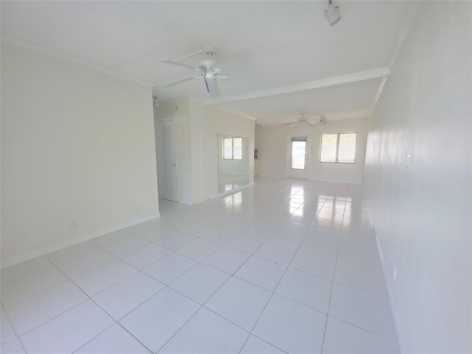 An empty living room features white tile flooring, two ceiling fans, and a mirrored wall — 2131 NE 42nd Court # 209e, Lighthouse Point FL 33064, LIGHTHOUSE POINT, FL