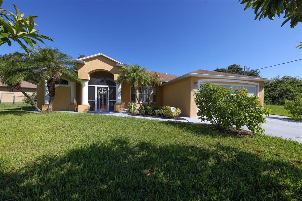 A single-story house with a tan stucco exterior, a front porch, and a two-car garage — 12004 SARTO LANE, NORTH PORT, FL
