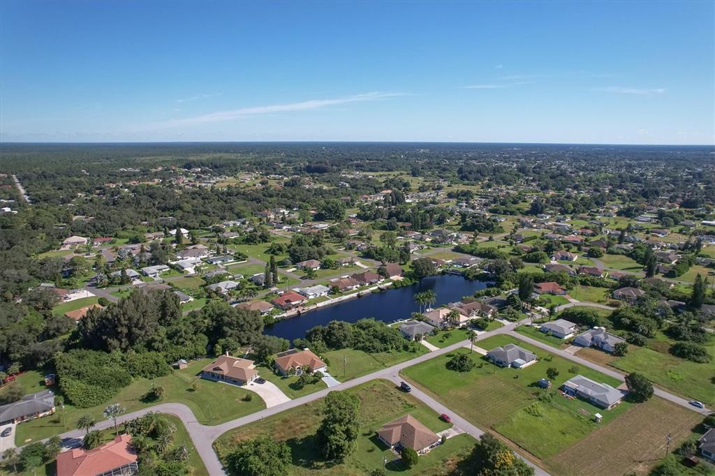 An aerial view shows a residential neighborhood with houses surrounding a central pond — 12004 SARTO LANE, NORTH PORT, FL