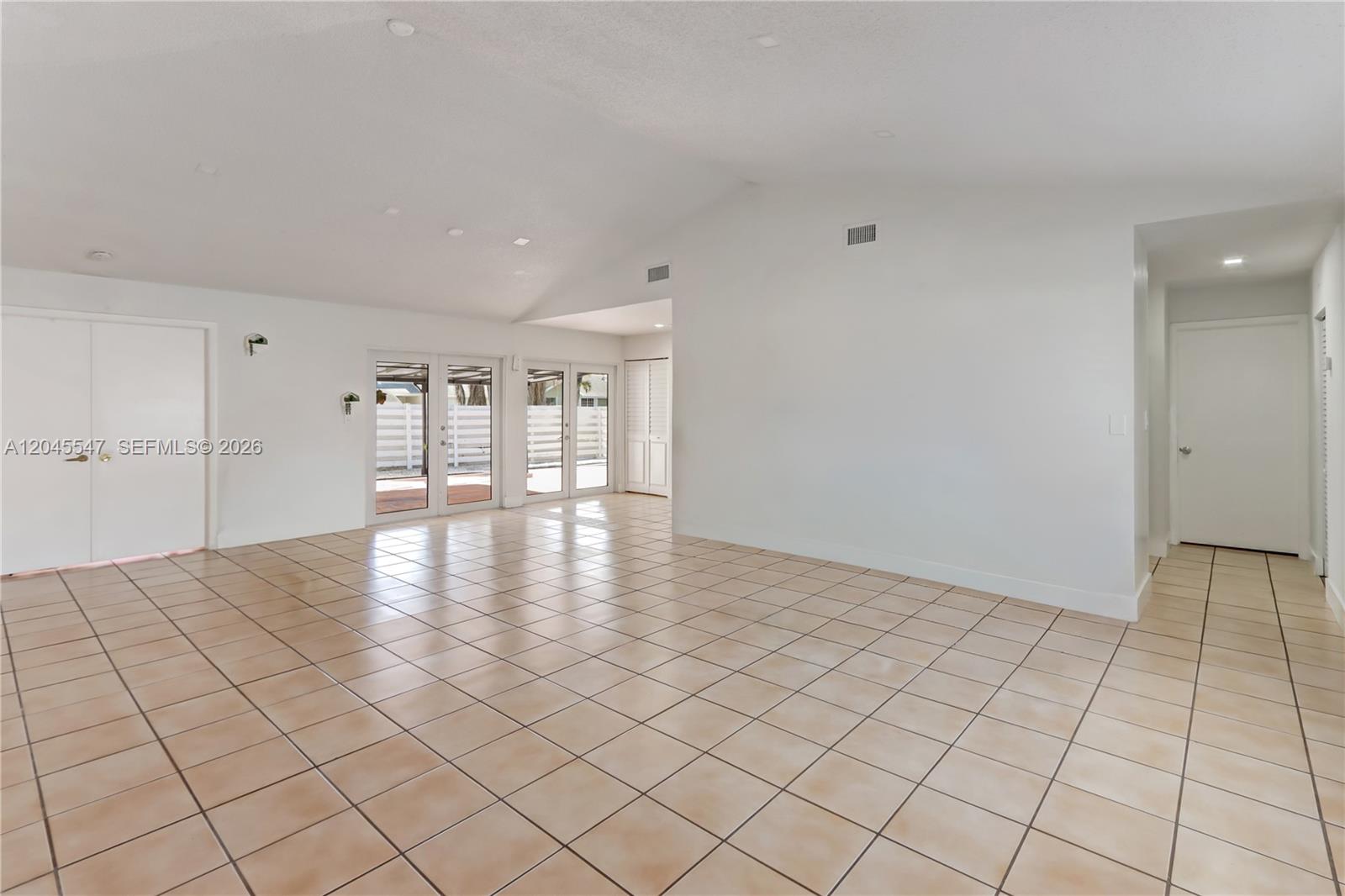 An empty room features white walls, beige tile flooring, and glass doors leading outside — 10125 SW 139th Pl, Miami FL 33186, MIAMI, FL