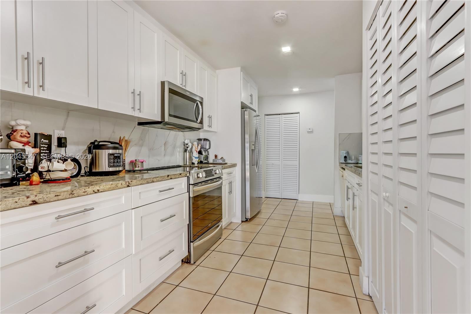 A kitchen features white cabinets, stainless steel appliances, granite countertops, and light-colored tile flooring — 10125 SW 139th Pl, Miami FL 33186, MIAMI, FL