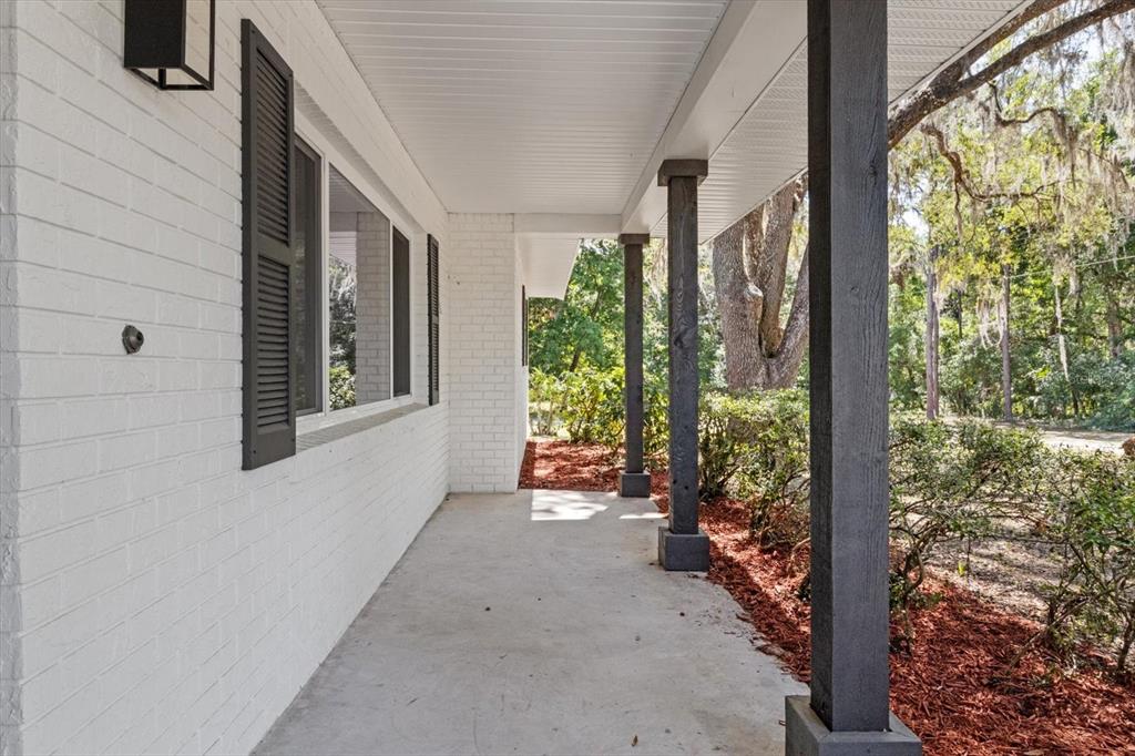 A covered concrete porch features white brick walls, dark shutters, and dark wooden support columns — 1255 S ESTATE POINT, INVERNESS, FL