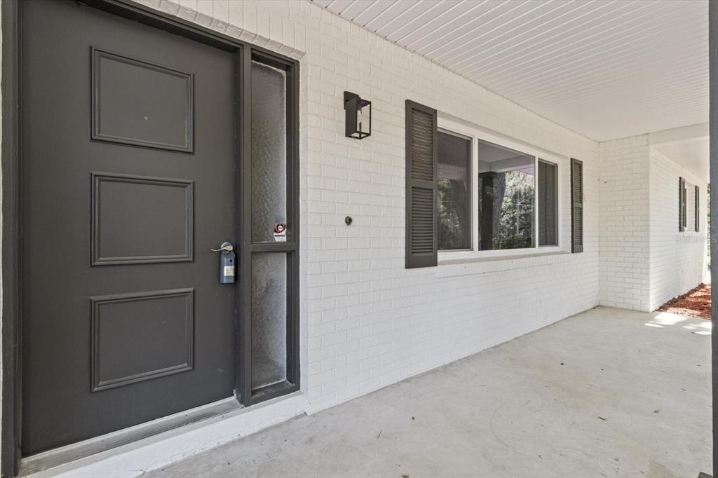 A white brick exterior wall features a dark front door and a window with shutters — 1255 S ESTATE POINT, INVERNESS, FL