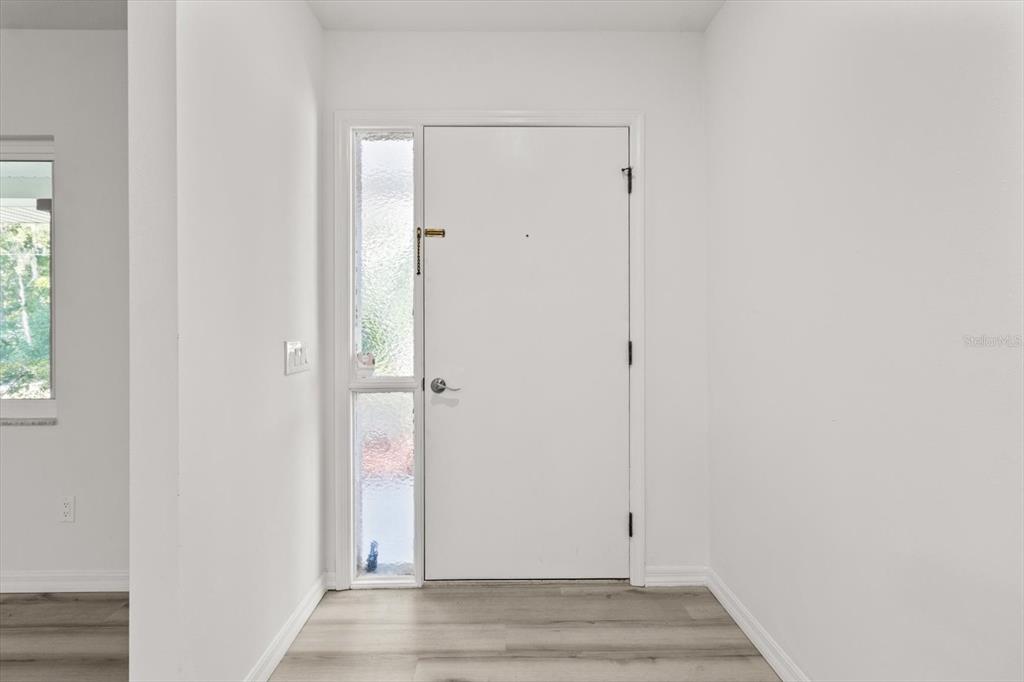 An entryway features a white front door with a vertical sidelight and light wood flooring — 1255 S ESTATE POINT, INVERNESS, FL