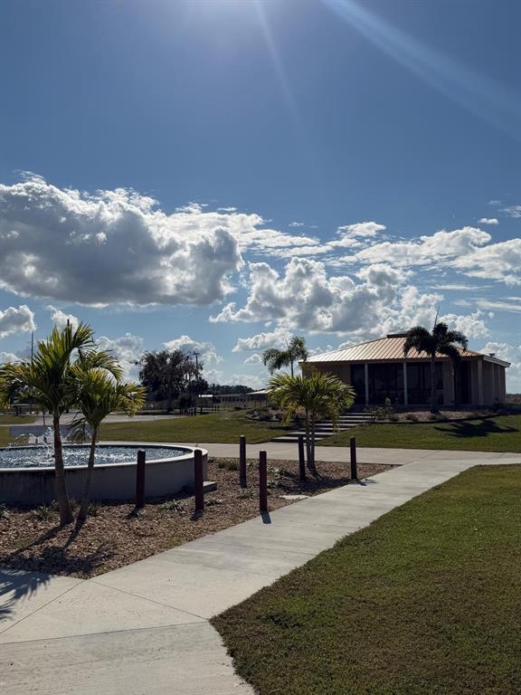 A concrete walkway leads to a building with a metal roof near a circular fountain — 405 BOUGAINVILLE DRIVE, INDIAN LAKE ESTATES, FL