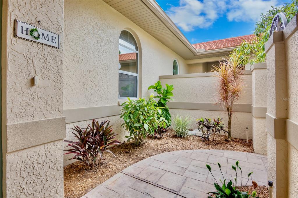 A paved walkway leads to a small courtyard with various plants and a stucco wall — 3386 CHELMSFORD COURT UNIT 7, SARASOTA, FL