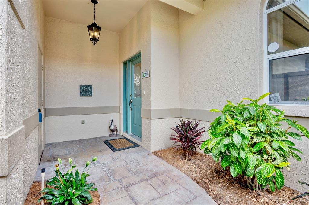 A covered entryway features a teal front door, stone-look pavers, and two potted plants — 3386 CHELMSFORD COURT UNIT 7, SARASOTA, FL