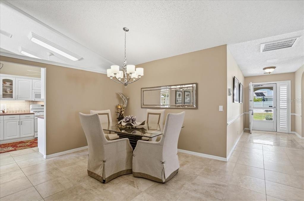 A dining area with a glass table, four upholstered chairs, and a chandelier — 4904 61ST AVENUE TERRACE W, BRADENTON, FL