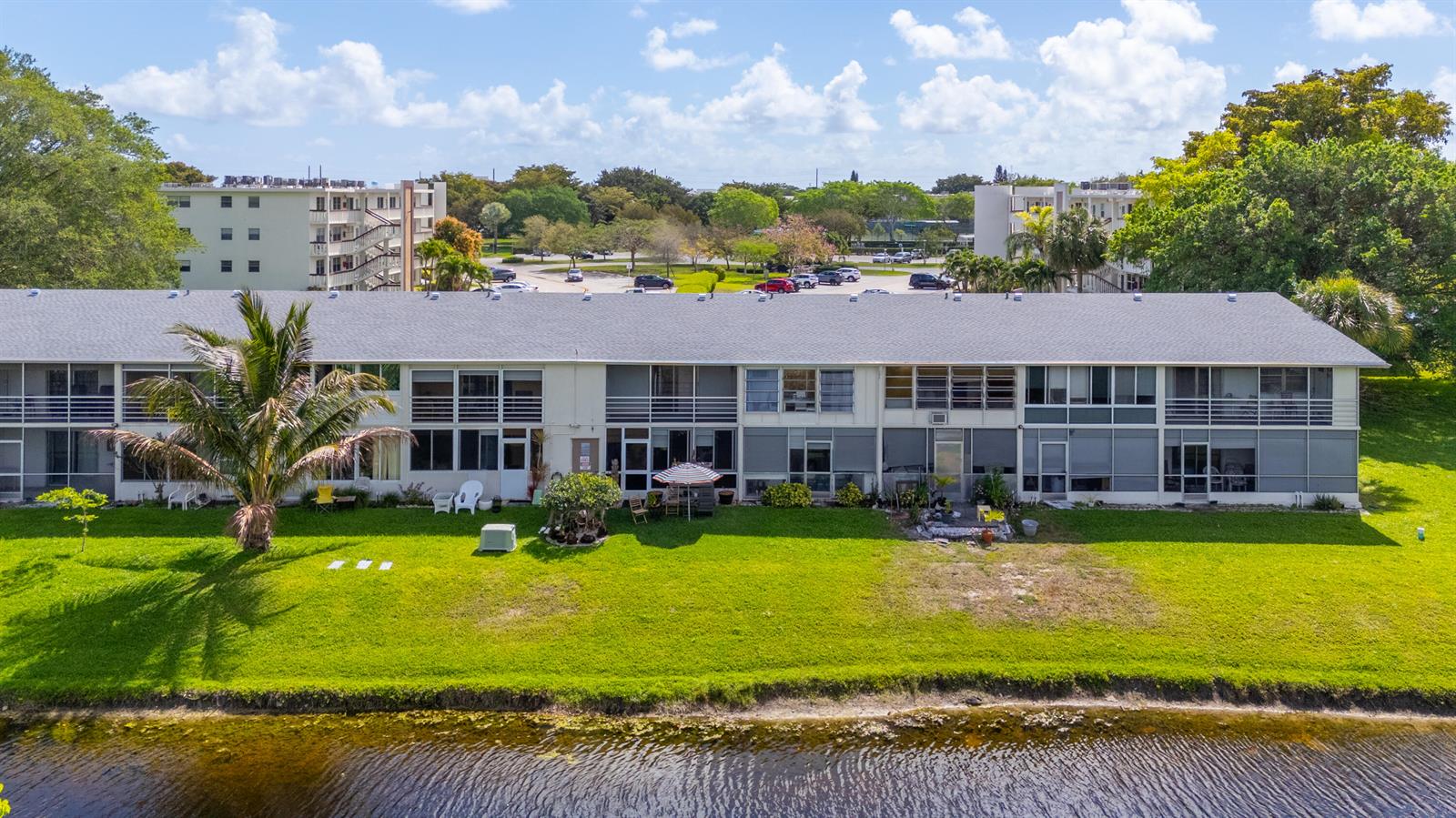 An aerial view shows a long, multi-story apartment building with screened balconies facing a pond — 72 Ashby B, Deerfield Beach FL 33442, DEERFIELD BEACH, FL