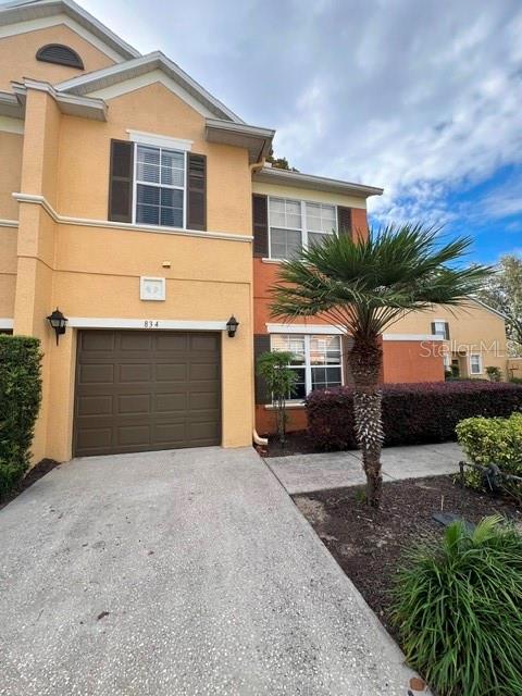 A two-story townhouse with a tan stucco exterior, a single-car garage, and a palm tree — 834 ASSEMBLY CT, REUNION, FL