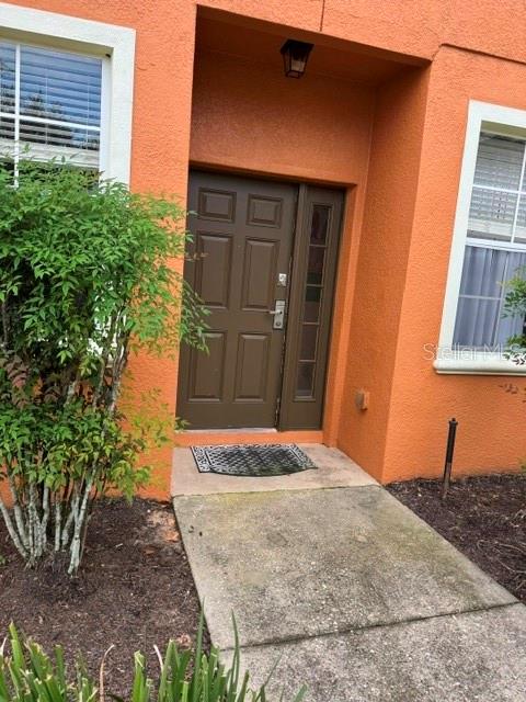 The exterior of a house features an orange stucco wall, a brown front door, and windows — 834 ASSEMBLY CT, REUNION, FL