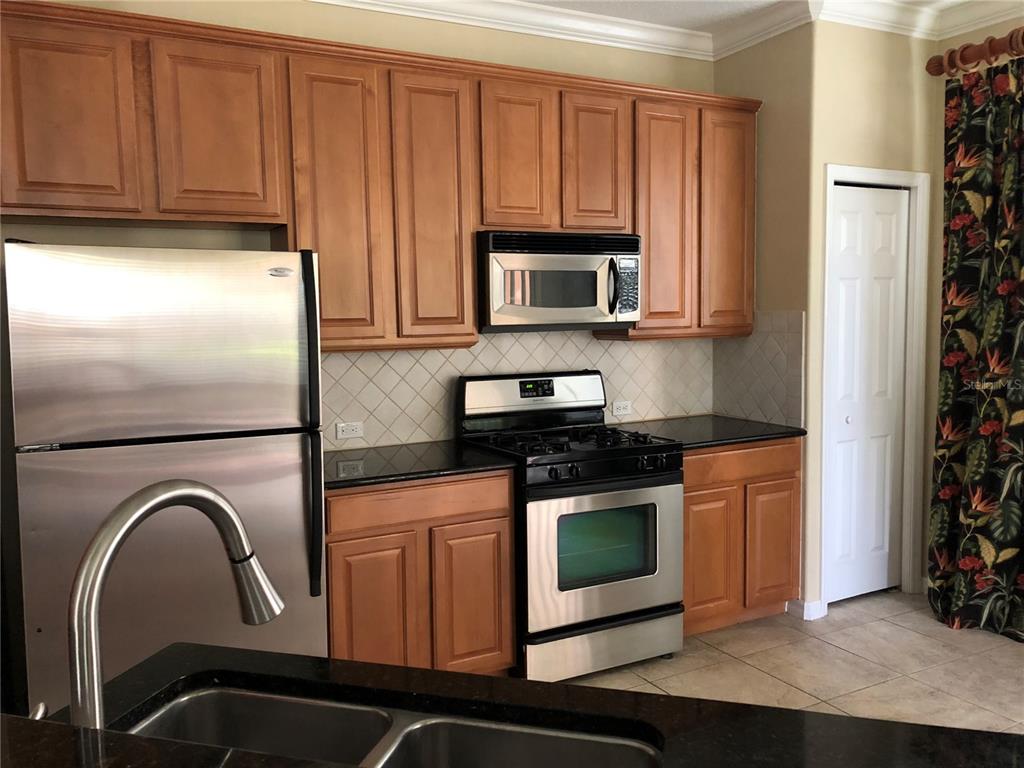 A kitchen features wood cabinets, stainless steel appliances, black countertops, and a tile backsplash — 834 ASSEMBLY CT, REUNION, FL