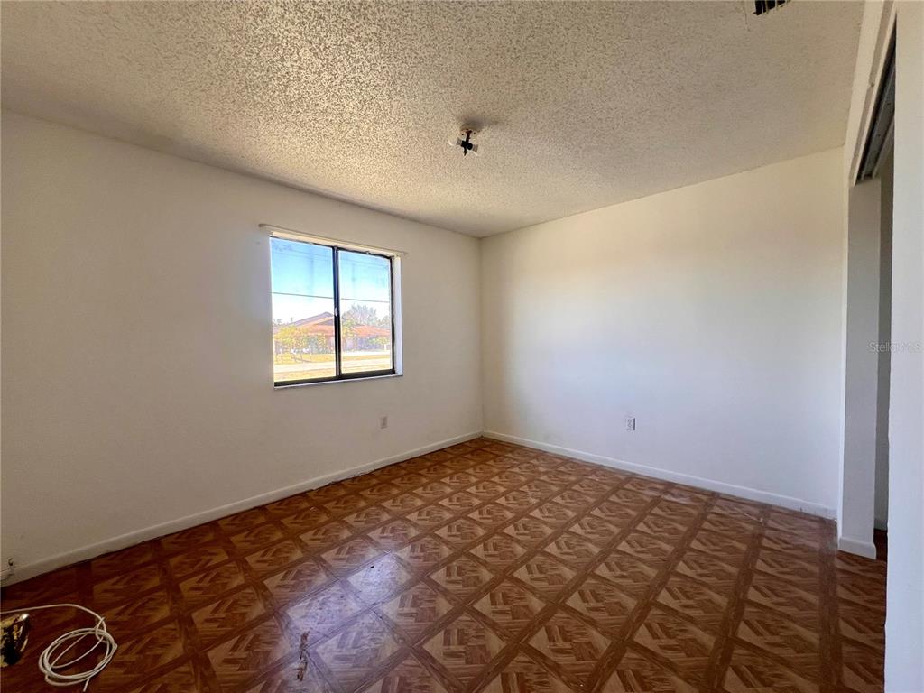 An empty bedroom features white walls, a popcorn ceiling, and patterned parquet wood flooring — 3847 JANEEN CIRCLE, MULBERRY, FL