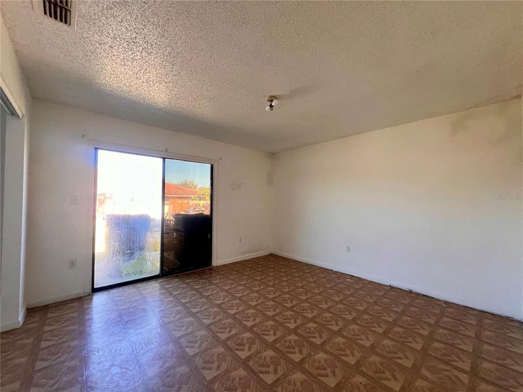 An empty room features patterned vinyl flooring, white walls, and a sliding glass patio door — 3847 JANEEN CIRCLE, MULBERRY, FL