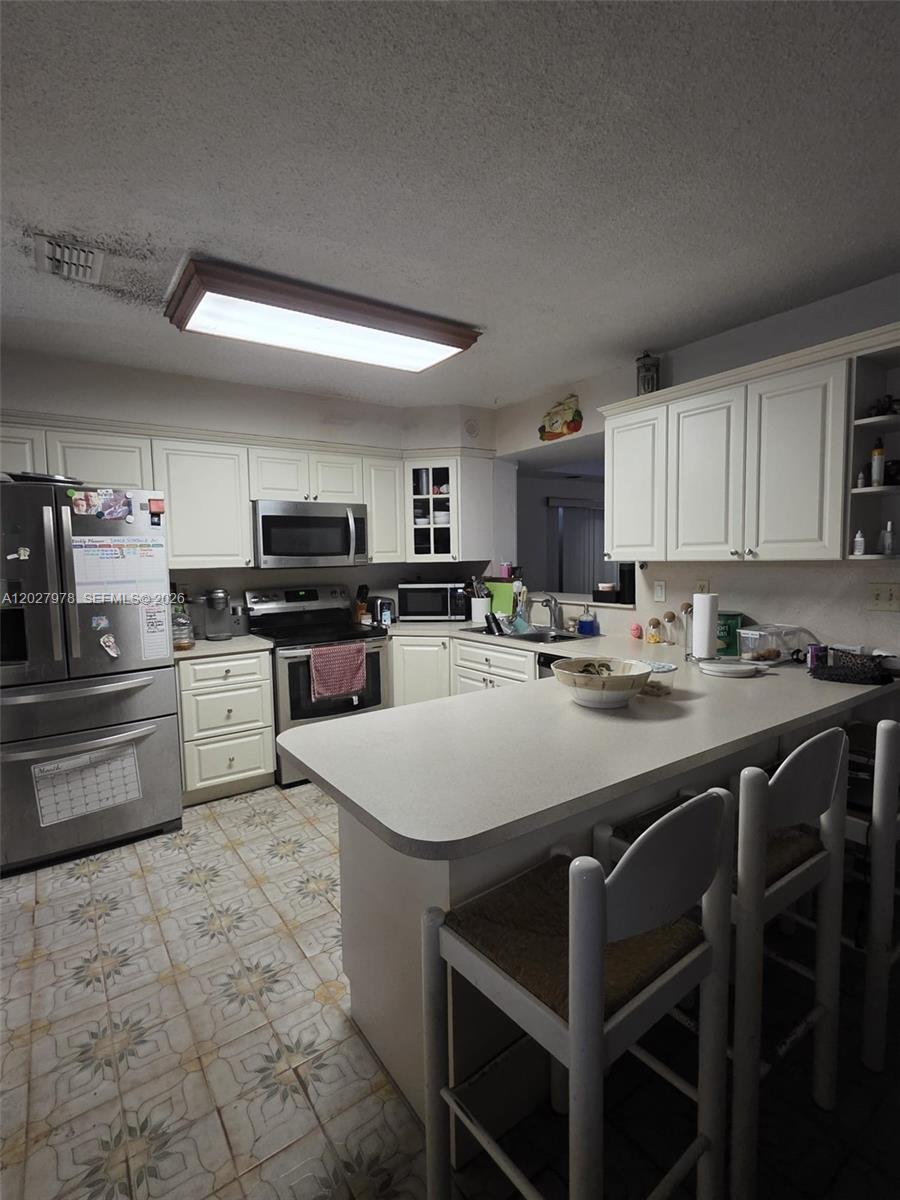 A kitchen features white cabinets, stainless steel appliances, a breakfast bar, and patterned tile flooring — 16825 NW 74th Ave, Hialeah FL 33015, HIALEAH, FL