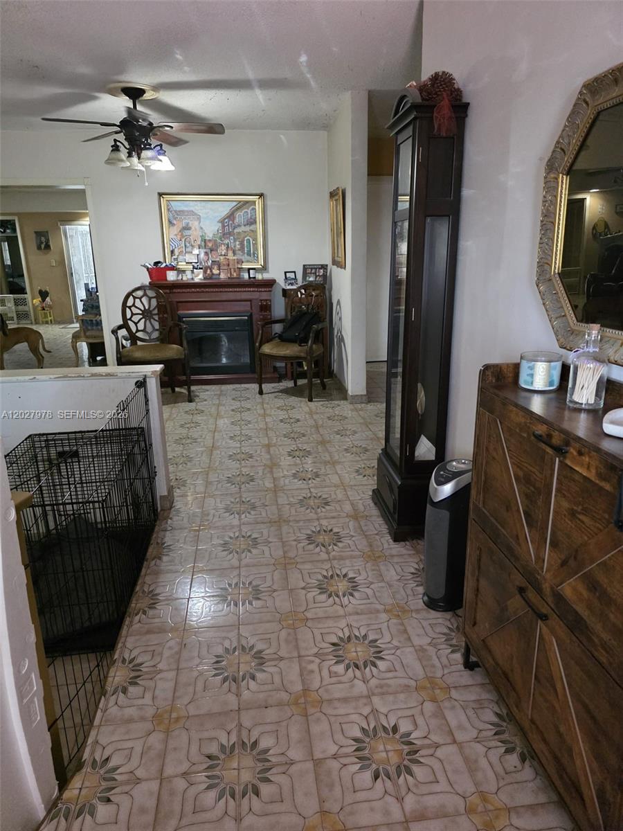 A tiled hallway leads to a fireplace, two chairs, and a tall wooden display cabinet — 16825 NW 74th Ave, Hialeah FL 33015, HIALEAH, FL
