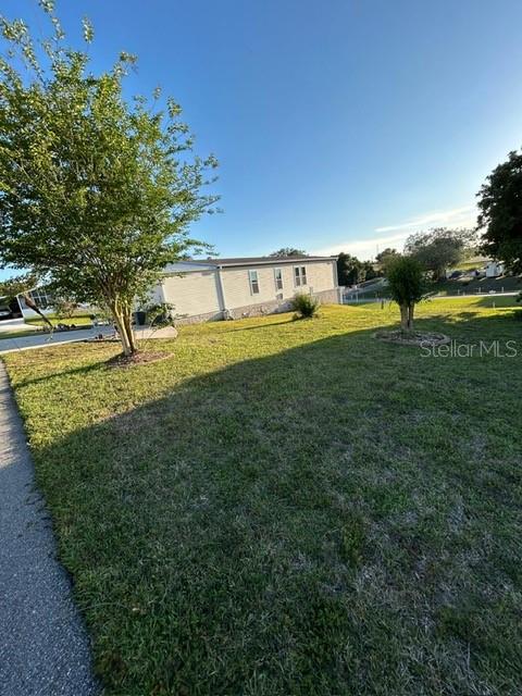 A single-story manufactured home sits on a grassy lot with two trees in the foreground — 354 EDGEWOOD, LAKE WALES, FL