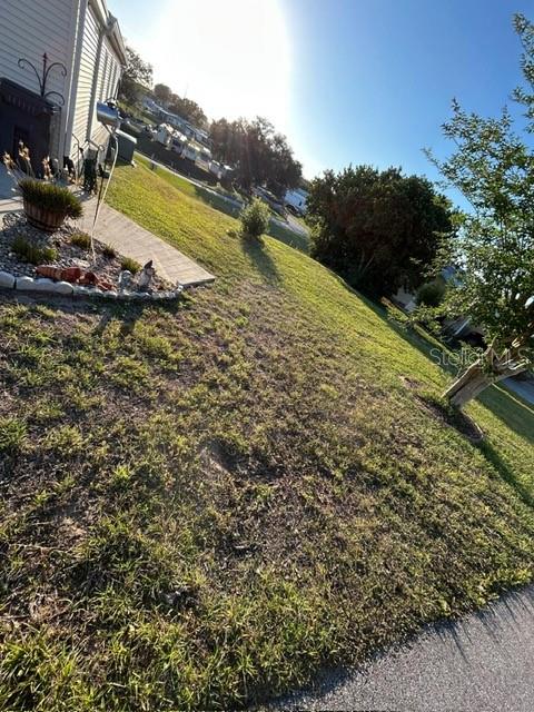 A grassy yard slopes upward toward a house with a small garden bed — 354 EDGEWOOD, LAKE WALES, FL