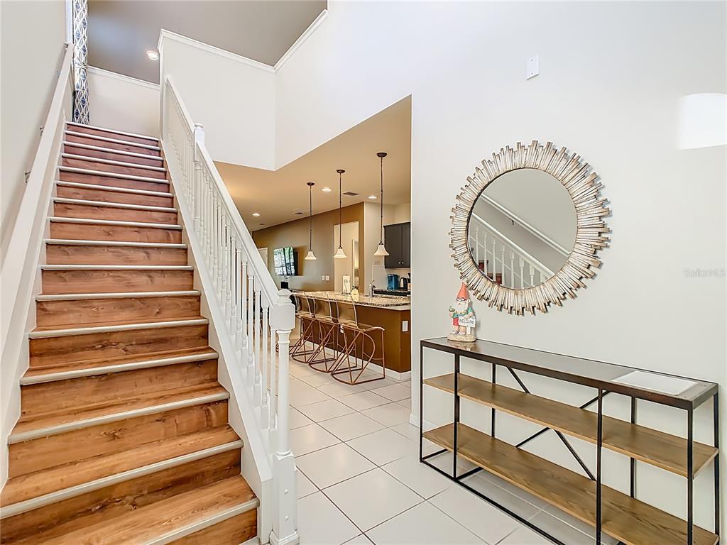 A staircase with wood treads leads to an upper level beside a kitchen with stools — 1809 NICE COURT, KISSIMMEE, FL