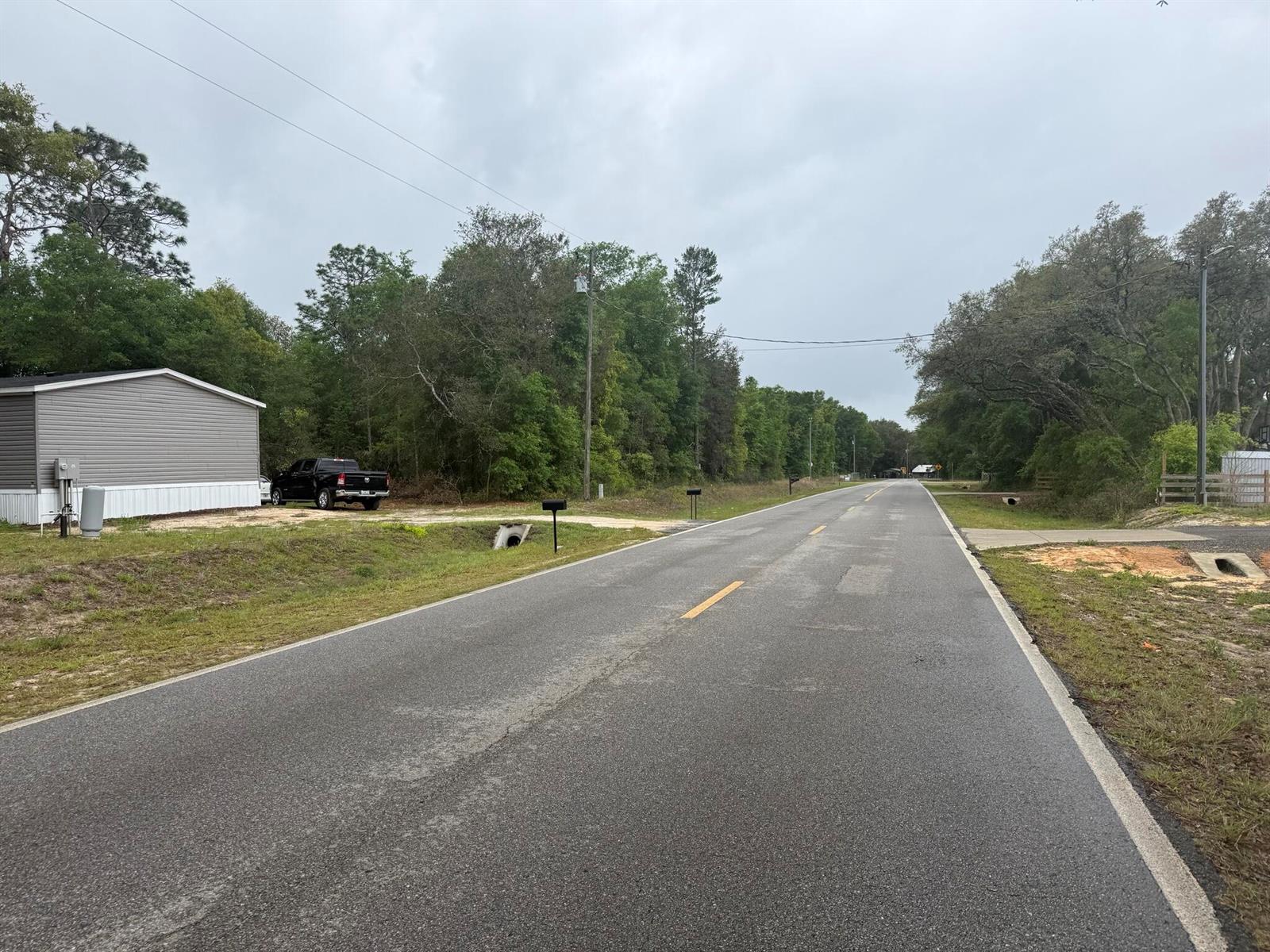 A paved road stretches into the distance, flanked by trees, a house, and roadside drainage culverts — Tbd Dawn Avenue, FL 32148, FL