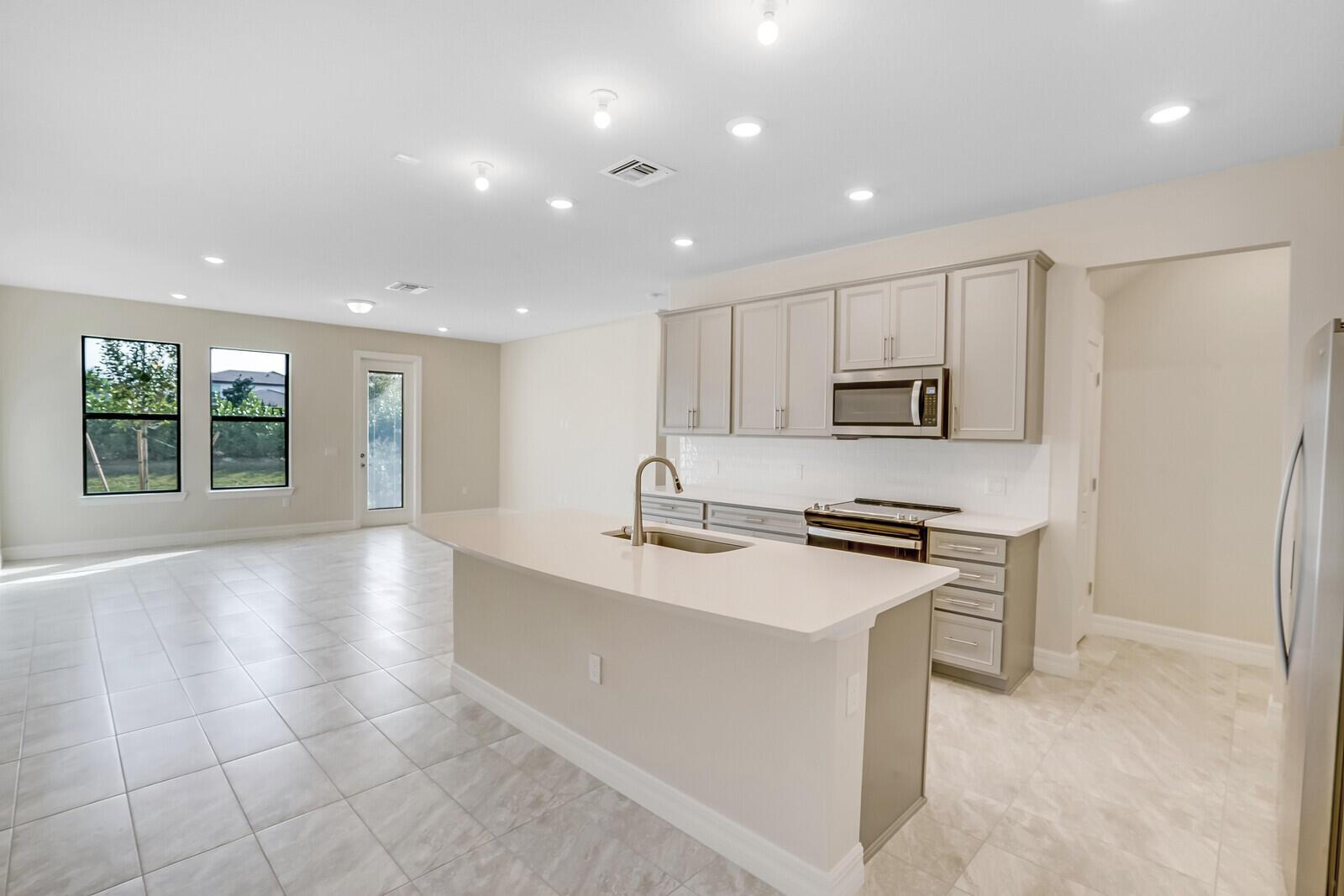 A kitchen with light gray cabinets, a quartz island, and tile flooring in an open space — 8656 Escue Street, Lake Worth FL 33467, LAKE WORTH, FL