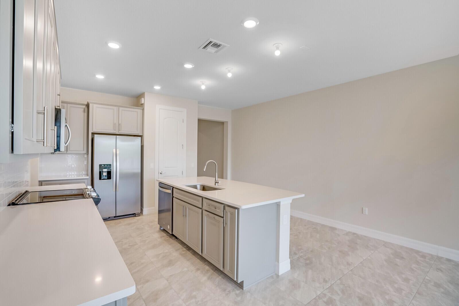 A modern kitchen features light gray cabinets, a central island with a sink, and tile flooring — 8656 Escue Street, Lake Worth FL 33467, LAKE WORTH, FL