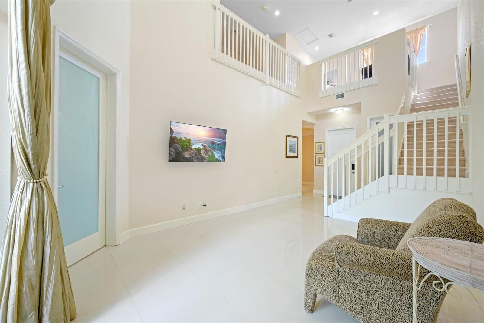 A high-ceilinged living room features white tile floors, a wall-mounted television, and a staircase — 1384 Harbor View W, Hollywood FL 33019, HOLLYWOOD, FL