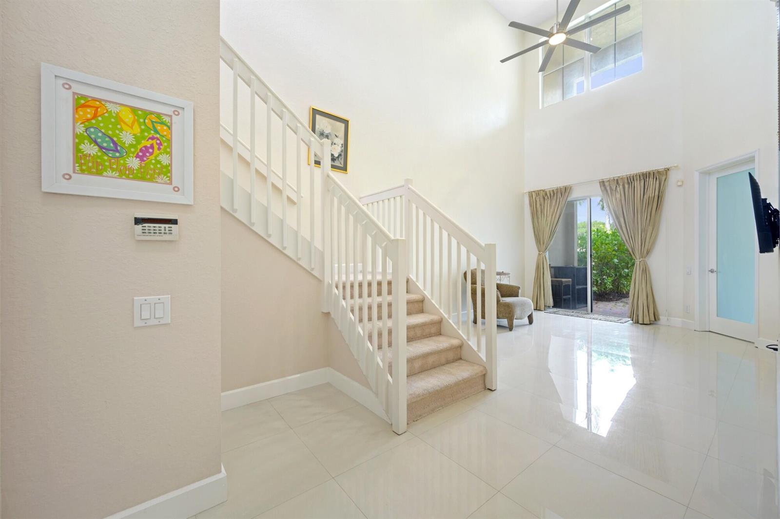 A bright entryway features white tile floors, a carpeted staircase, and a high ceiling — 1384 Harbor View W, Hollywood FL 33019, HOLLYWOOD, FL
