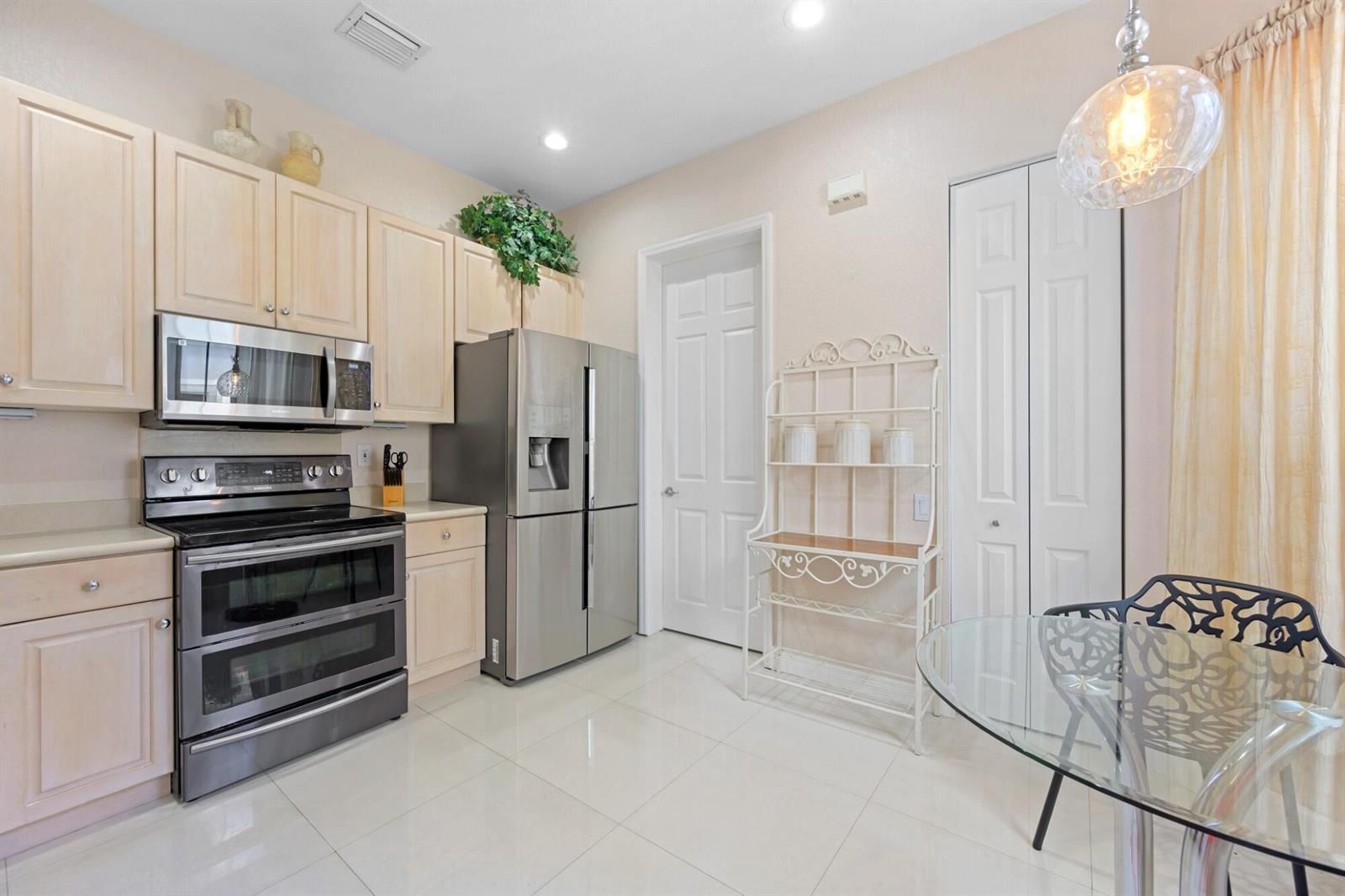 A kitchen features light wood cabinets, stainless steel appliances, tile flooring, and a dining area — 1384 Harbor View W, Hollywood FL 33019, HOLLYWOOD, FL