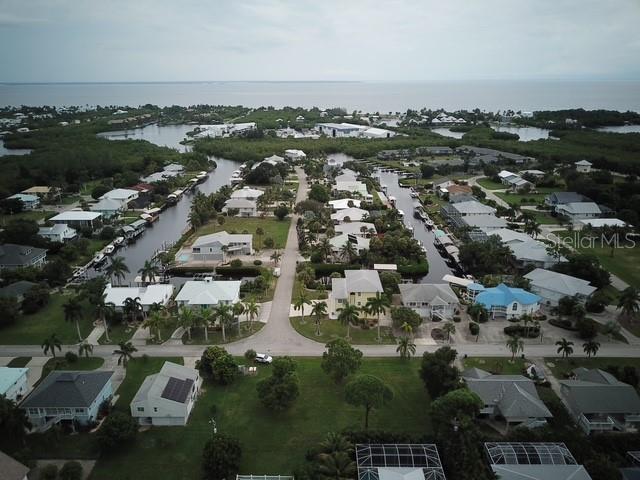 An aerial view shows a coastal residential neighborhood with houses, canals, and surrounding vegetation — 7883 BREAKWATER COURT, BOKEELIA, FL
