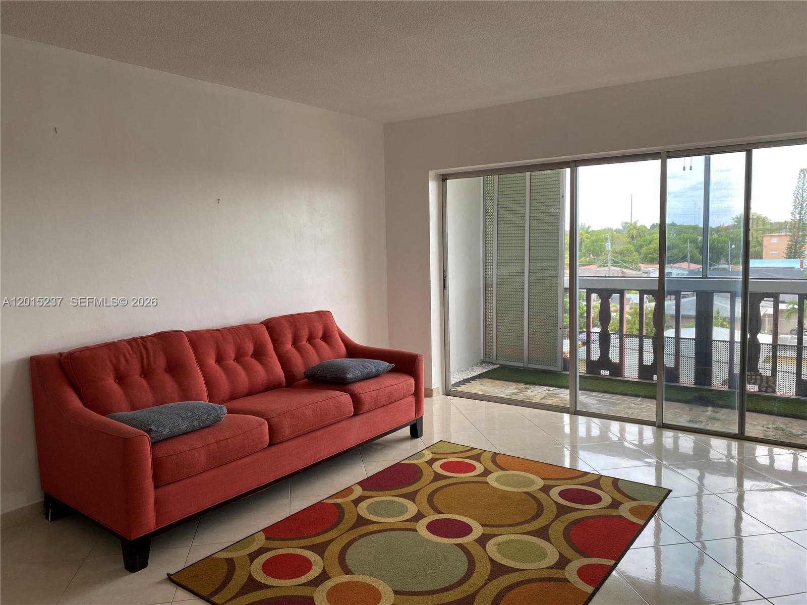 A living room features a red sofa, a patterned rug, and a sliding glass door — 215 SE 3rd Ave # 408C, Hallandale Beach FL 33009, HALLANDALE BEACH, FL