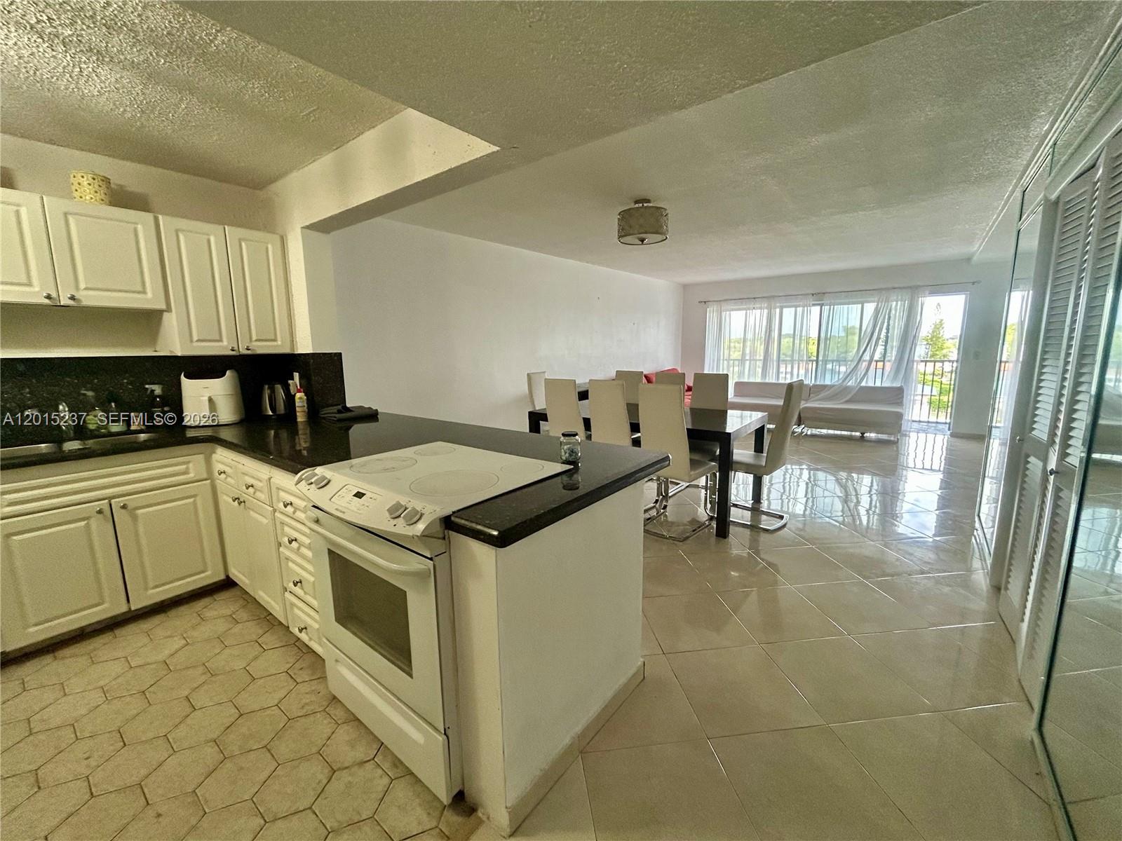 A kitchen with white cabinets and a black countertop opens into a dining and living area — 215 SE 3rd Ave # 408C, Hallandale Beach FL 33009, HALLANDALE BEACH, FL
