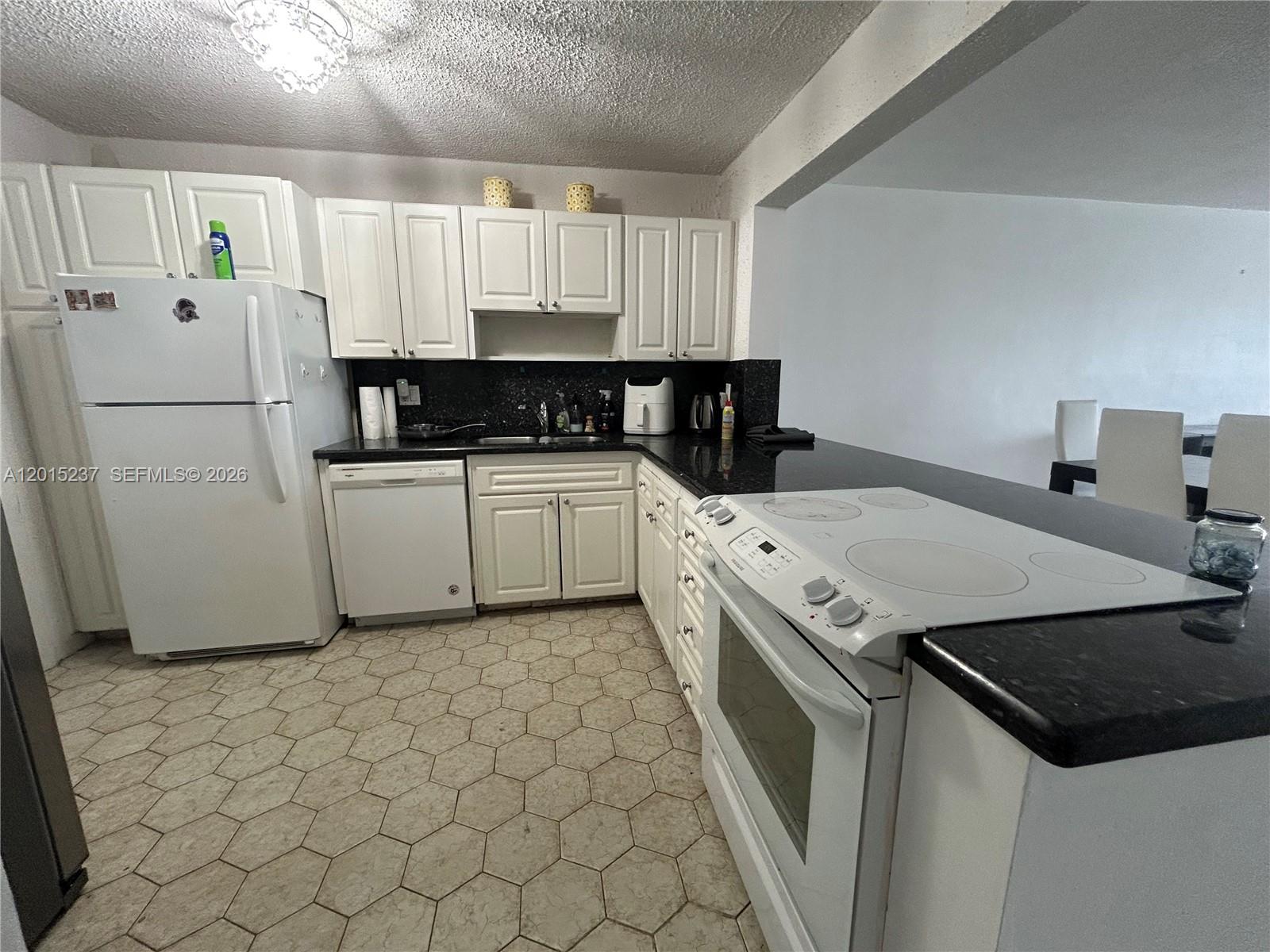 A kitchen features white cabinets, black countertops, white appliances, and hexagonal floor tiles — 215 SE 3rd Ave # 408C, Hallandale Beach FL 33009, HALLANDALE BEACH, FL