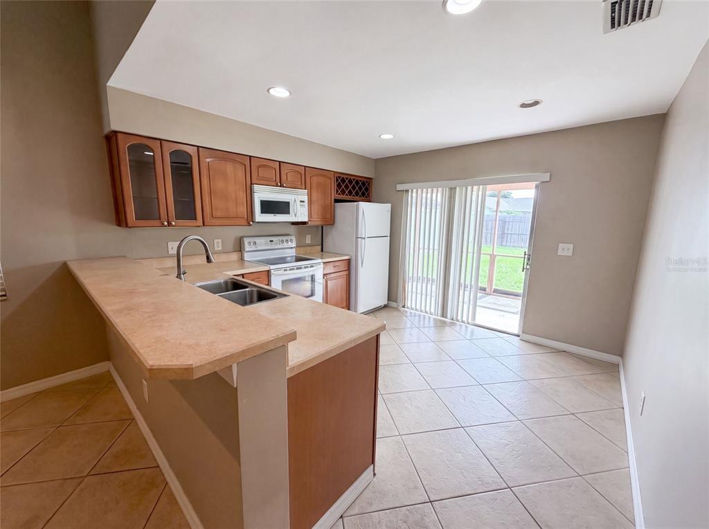 A kitchen with wood cabinets, laminate countertops, and tile flooring opens to a sliding glass door — 1393 SAN DIEGO COURT, WINTER SPRINGS, FL