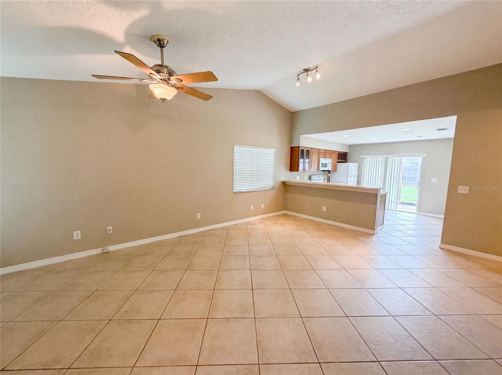 An open-concept living room with beige tile flooring, a ceiling fan, and a kitchen pass-through — 1393 SAN DIEGO COURT, WINTER SPRINGS, FL